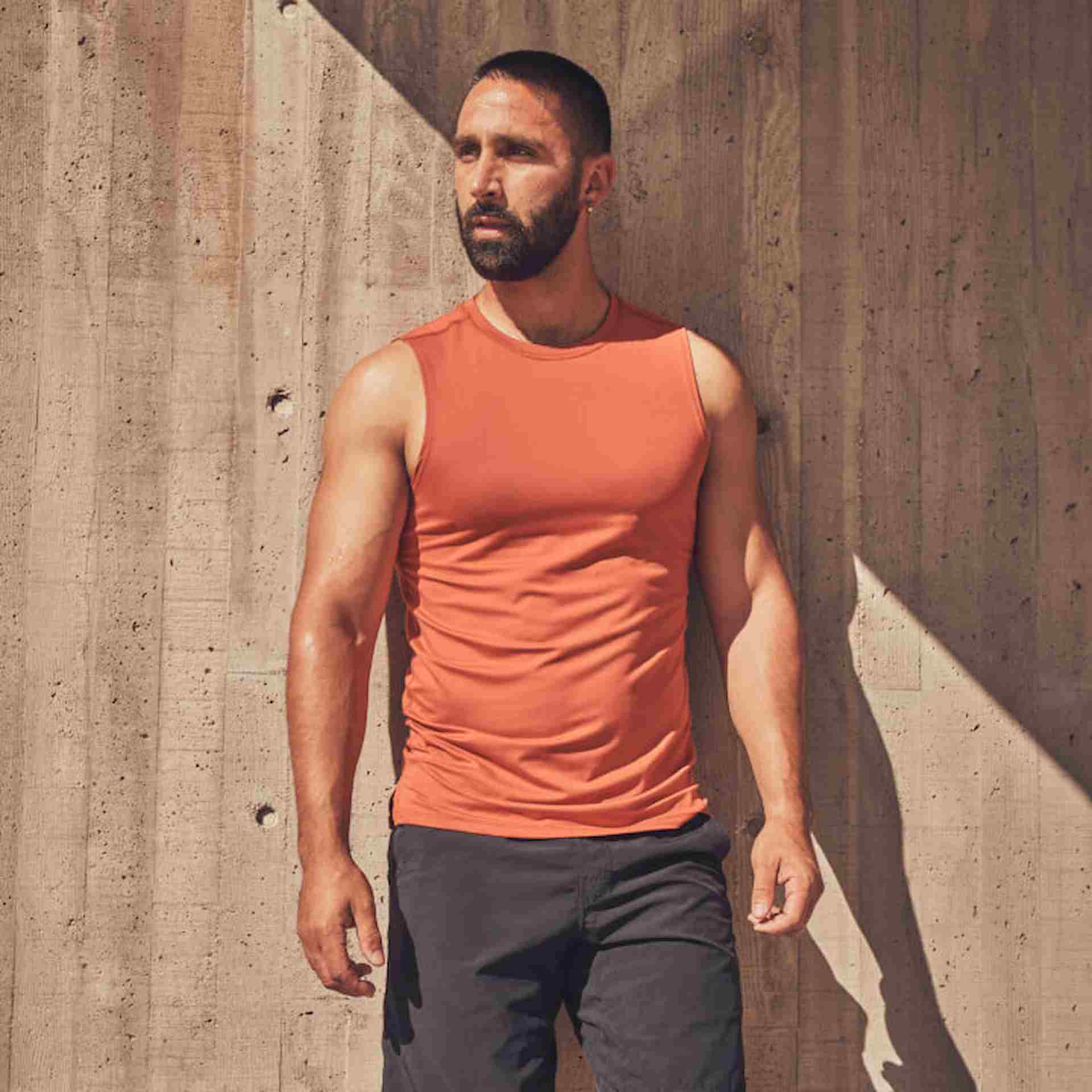 Male athlete wearing workout clothes leaning against cement wall