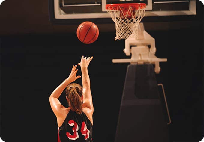 A basketball player wearing a black jersey with the number 34 is shooting a basketball towards the hoop in an indoor court. The ball is in mid-air, approaching the basket.