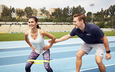 male NASM trainer assisting woman client with band one her legs