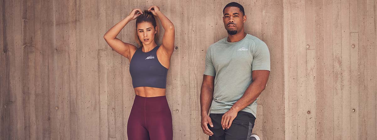 Female and male NASM trainers posing against cement wall