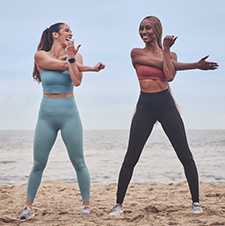 Two female NASM athletes stretching arms on beach