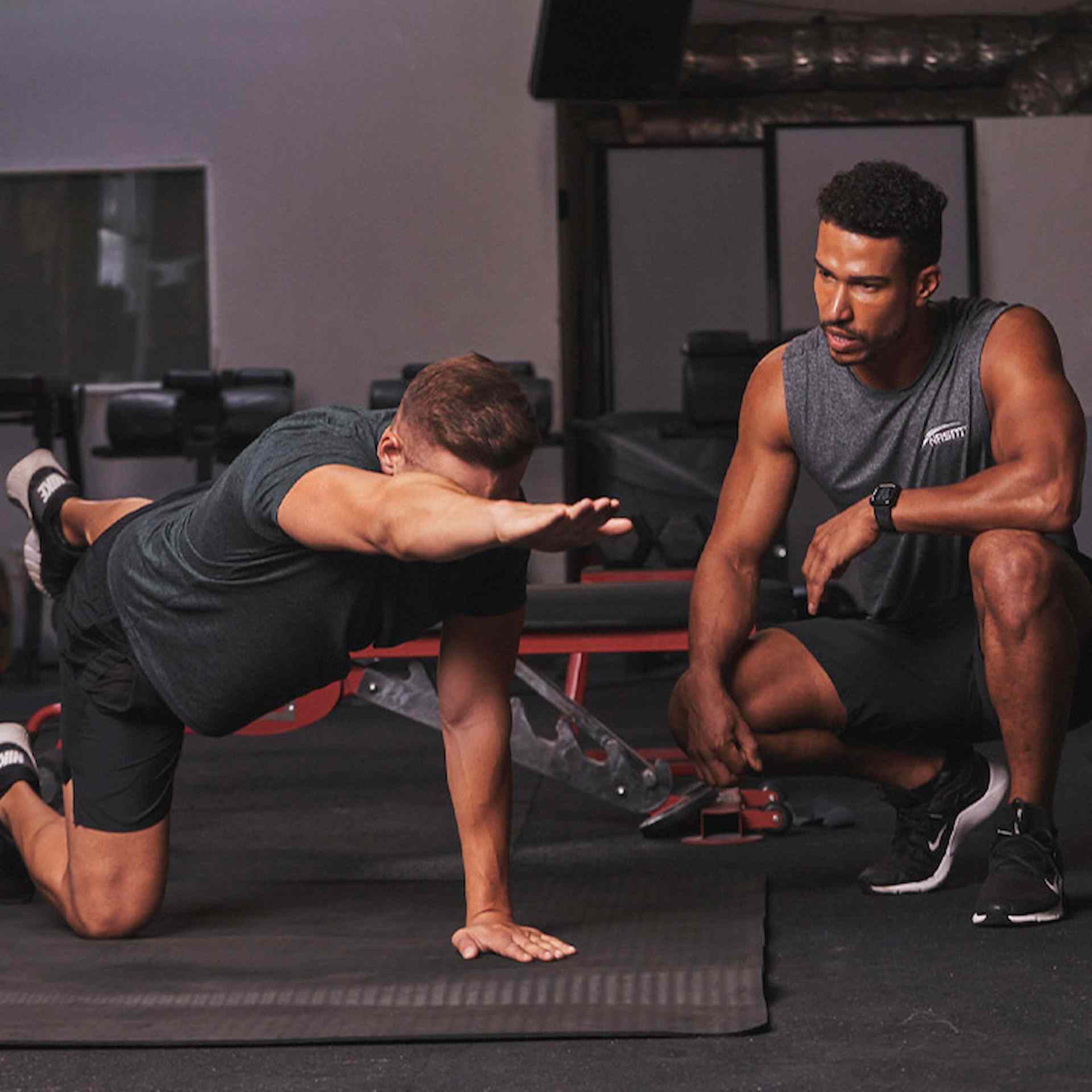 Male NASM trainer sitting next to client performing bird dog workout