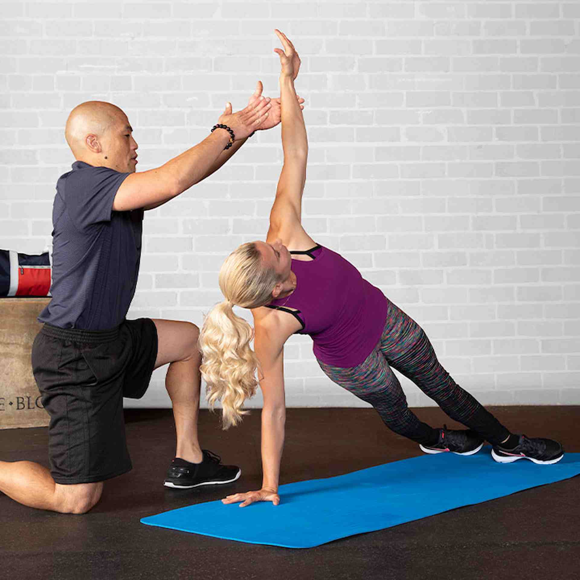 Male NASM trainer assisting female client in side plank with raised arm