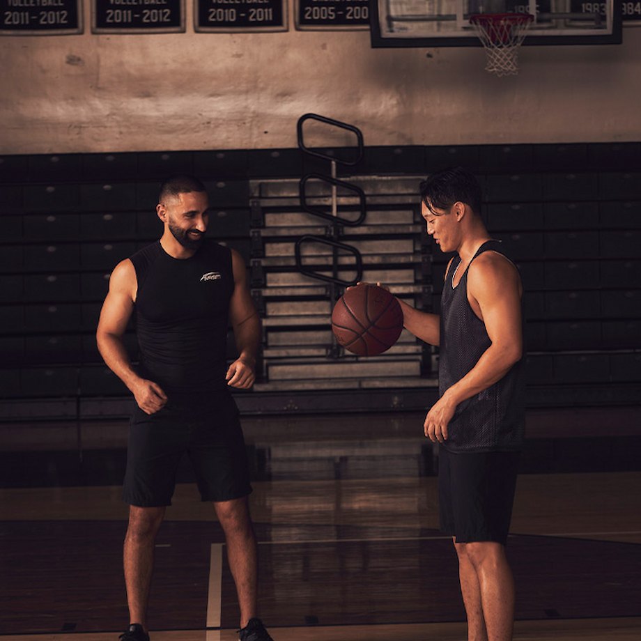 Male NASM trainer playing basketball with male athlete inside gymnasium