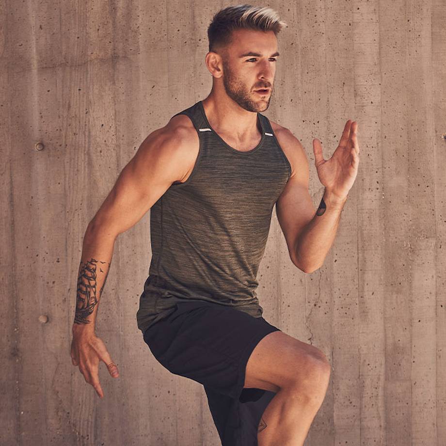 Male athlete doing cardio based workout outside with cement wall behind him