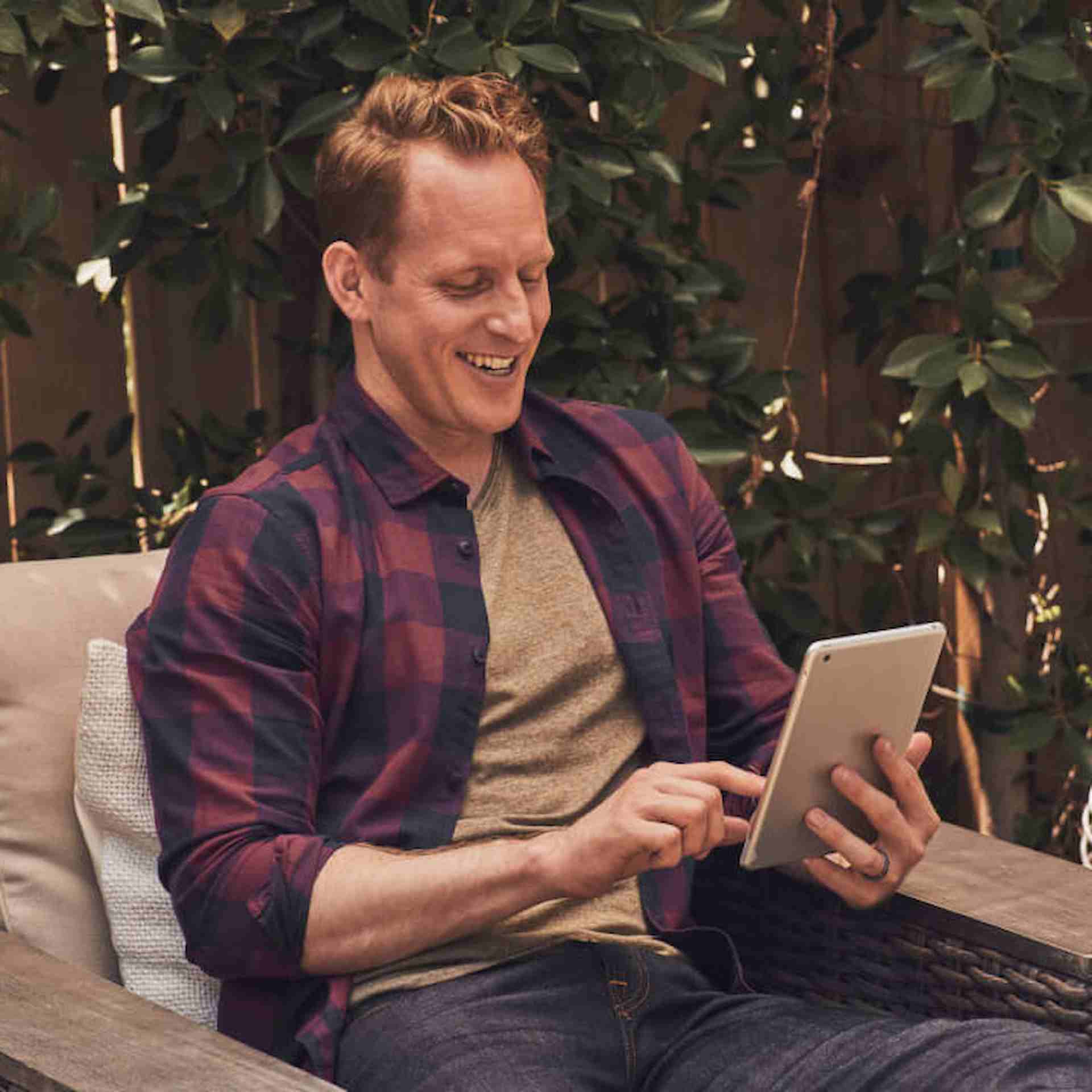 Male in flannel shirt sitting outside using tablet