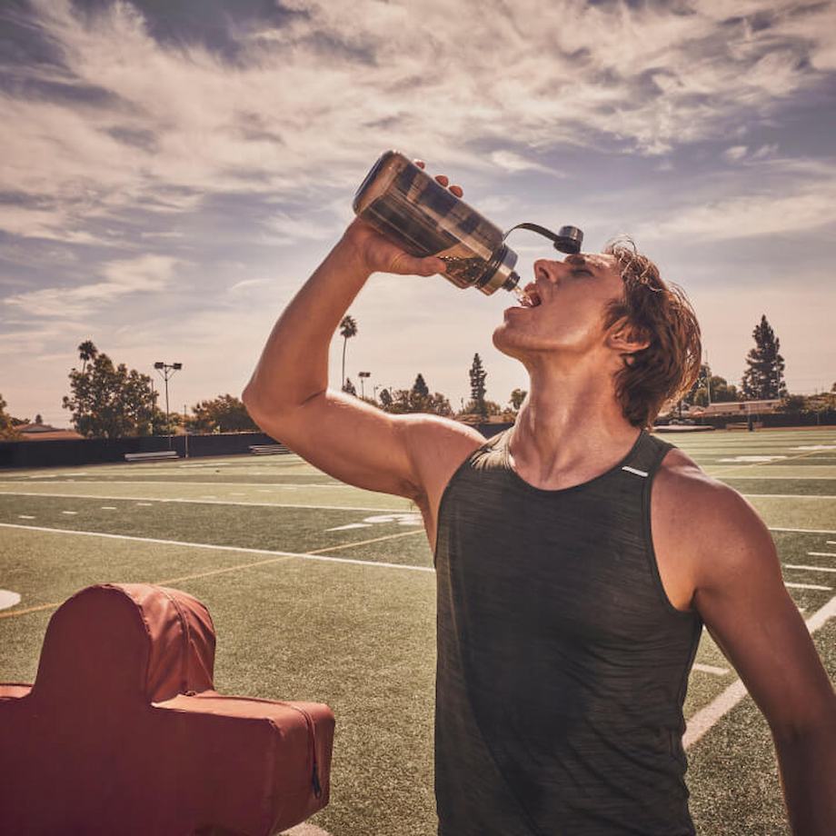 Male athlete drinking out of water bottle on football field