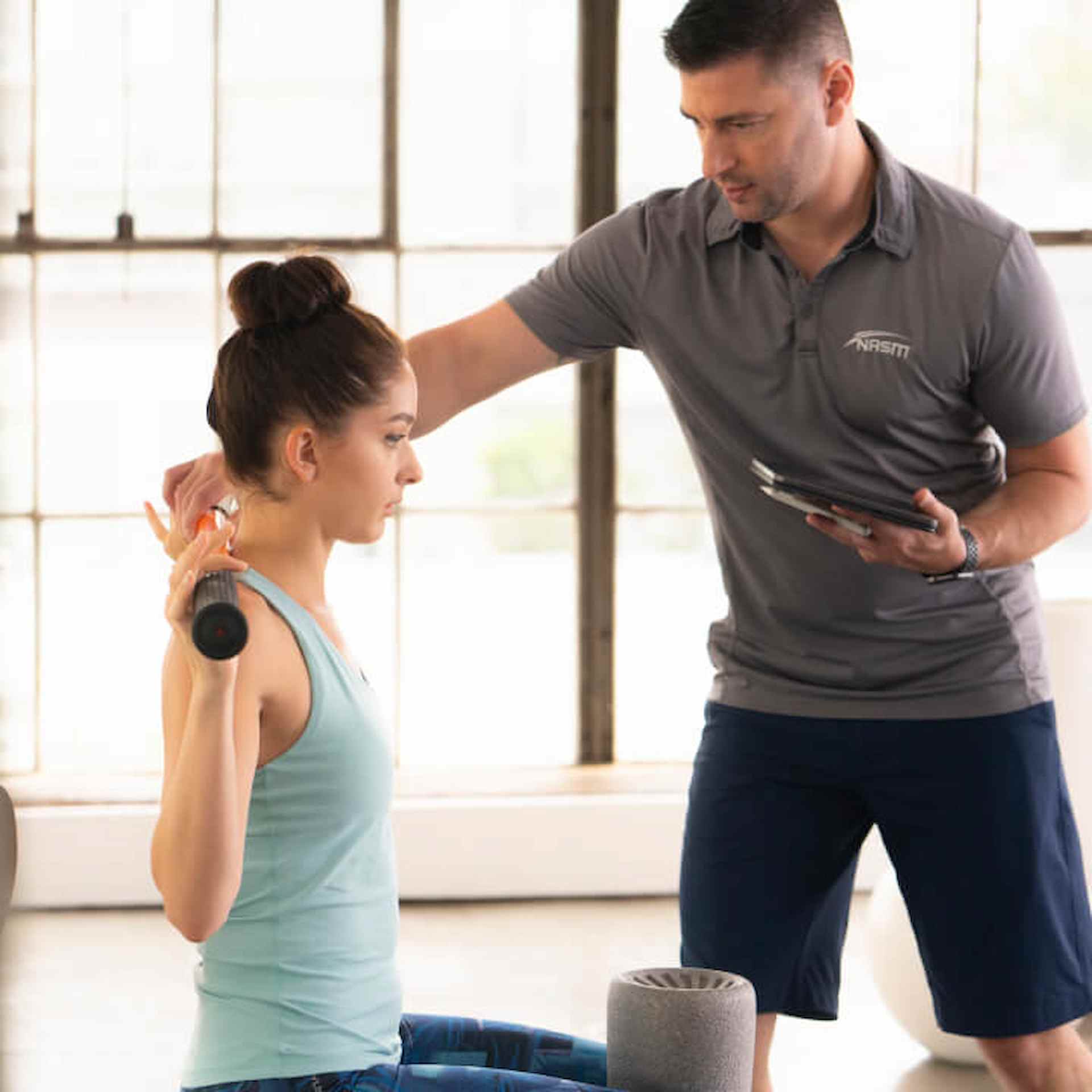 A male trainer assisting a female client in the gym 
