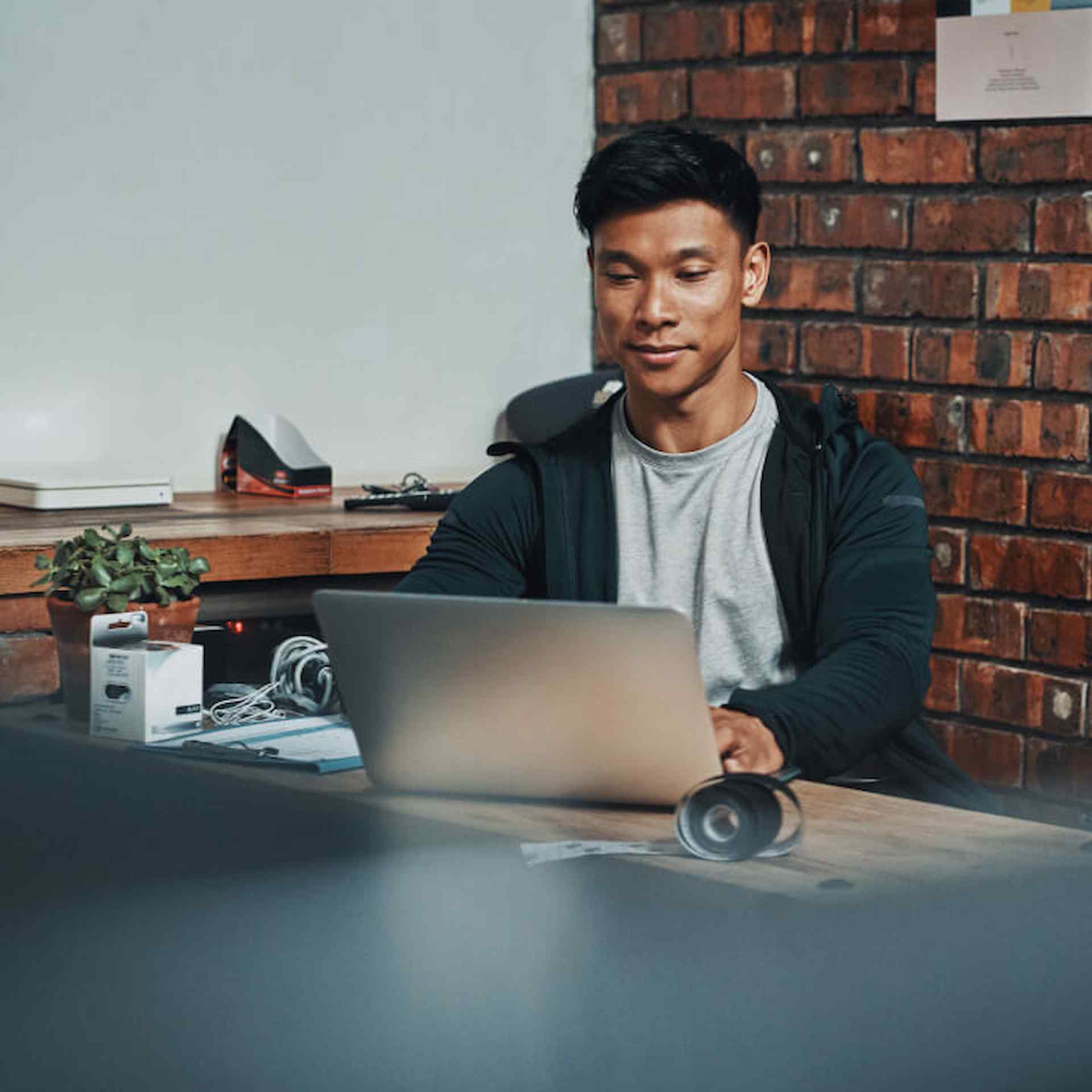 Male sitting on laptop at a desk with brick background