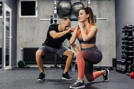 Male trainer assisting female client on back lunge workout