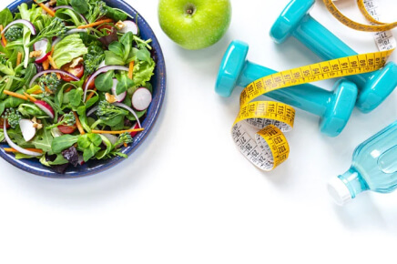 Bowl of salad with hand weights and water bottle