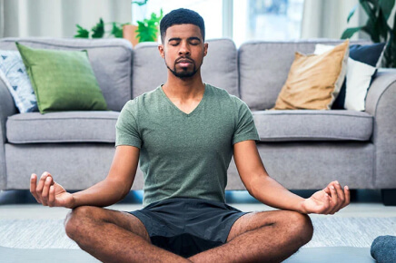 Male sitting in living room on yoga matt doing a meditation