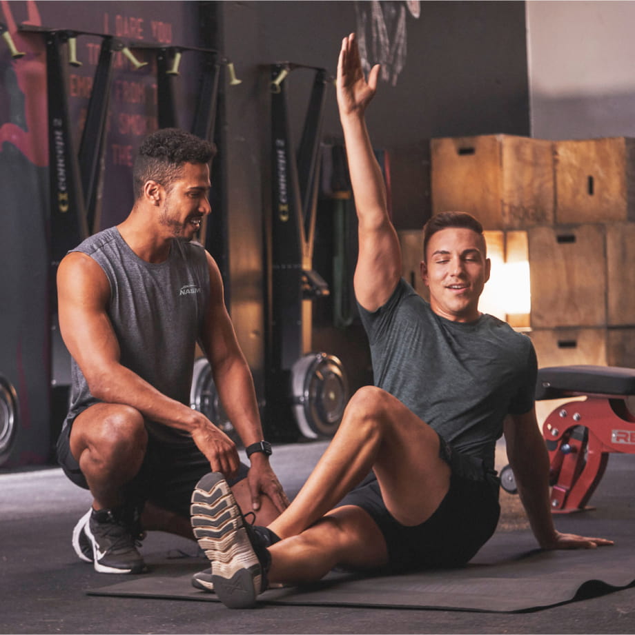 A male trainer helping a make client with stretching