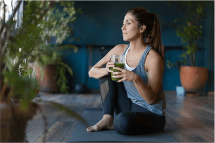 A lady sitting on a mat with a green smoothie