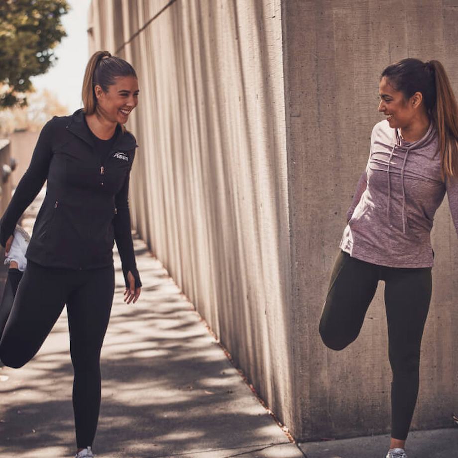 Female NASM trainer doing quad stretch with female client outside