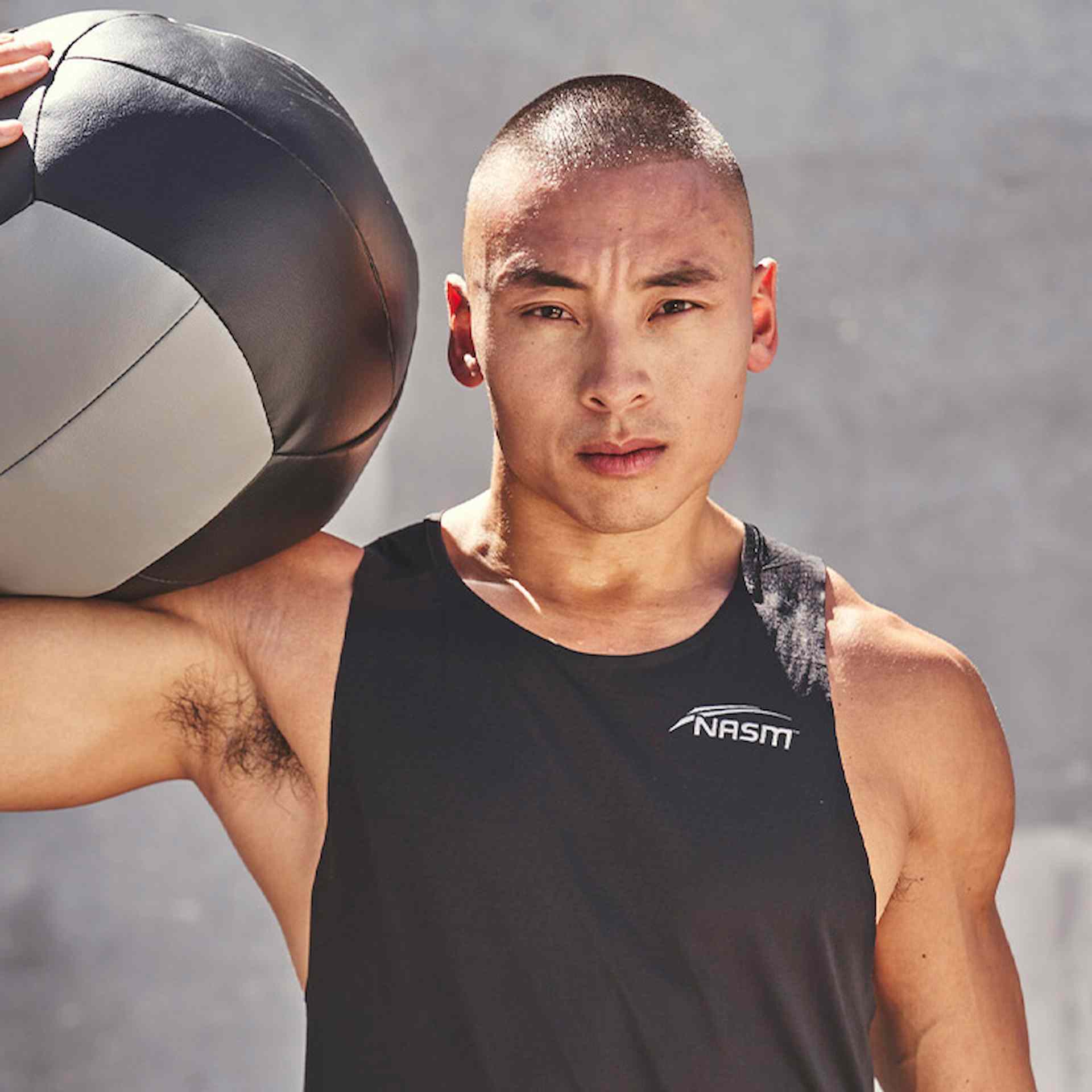 Male NASM trainer posing with weighted ball on shoulder