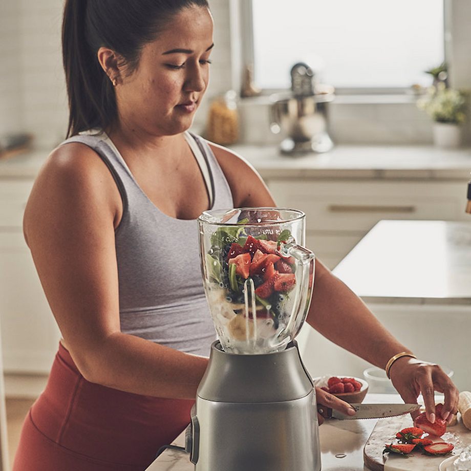 Female making smoothie with different fruits inside kitchen