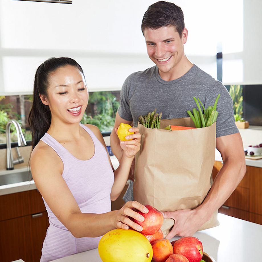 Male and female standing in kitchen unloading produce