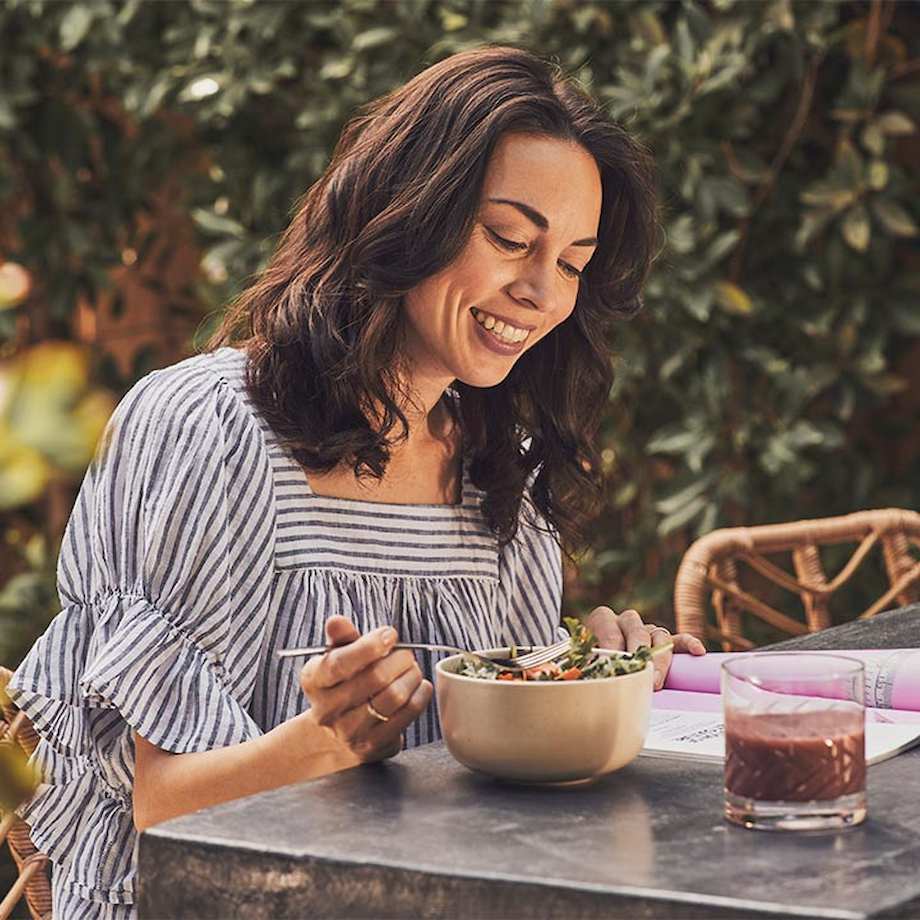 Female sitting outside eating salad and looking through nutrition book