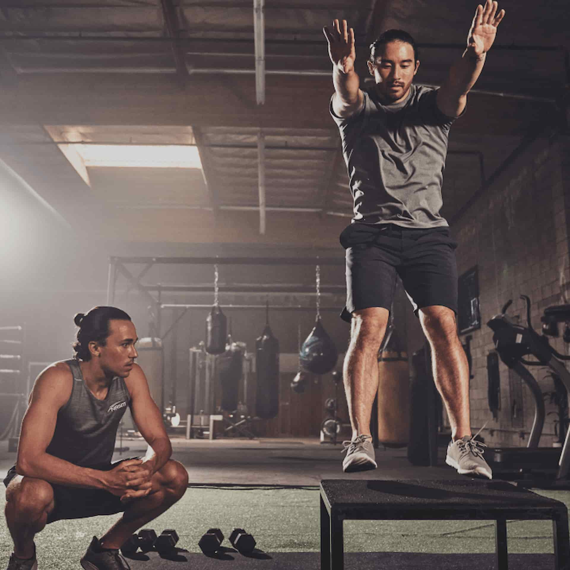 Male NASM trainer watching male client perform box jump