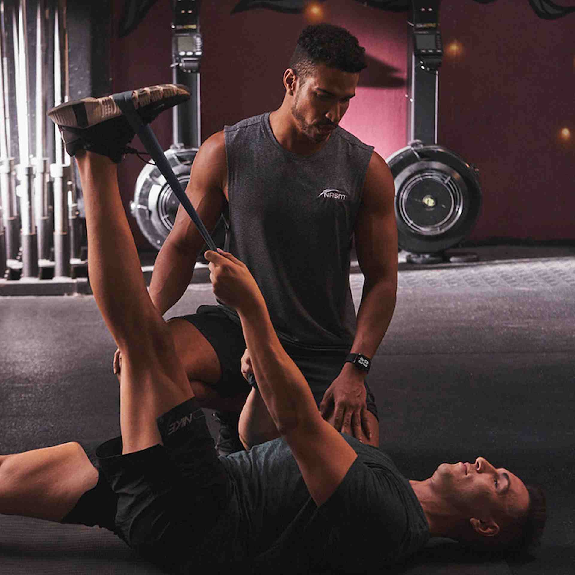 Male NASM trainer assisting male client on full leg stretch with band