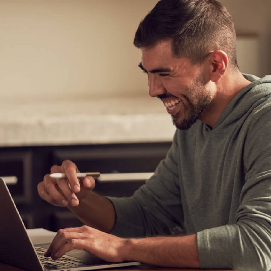 Male laughing while looking at laptop while sitting in kitchen