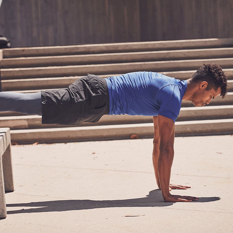 Male athlete doing elevated plank outside on cement bench