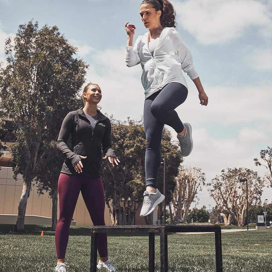 Female NASM coach training female client through box jump outside