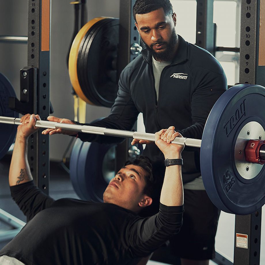 Male NASM trainer spotting male athlete on barbell chest lift