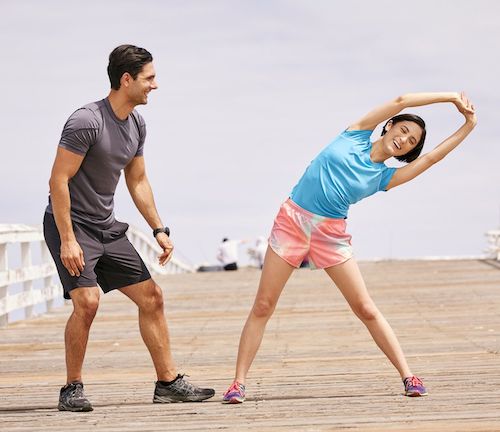 Male trainer standing next to female while doing side stretch