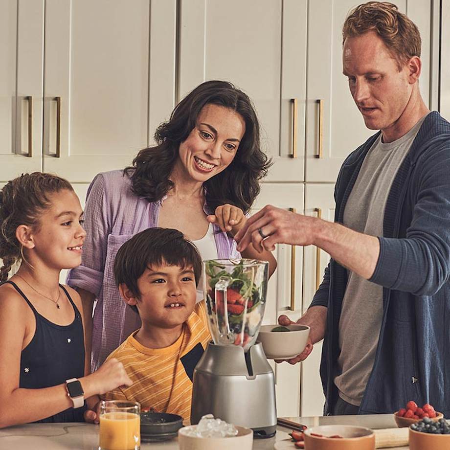 Parents making healthy smoothie with their two kids inside kitchen