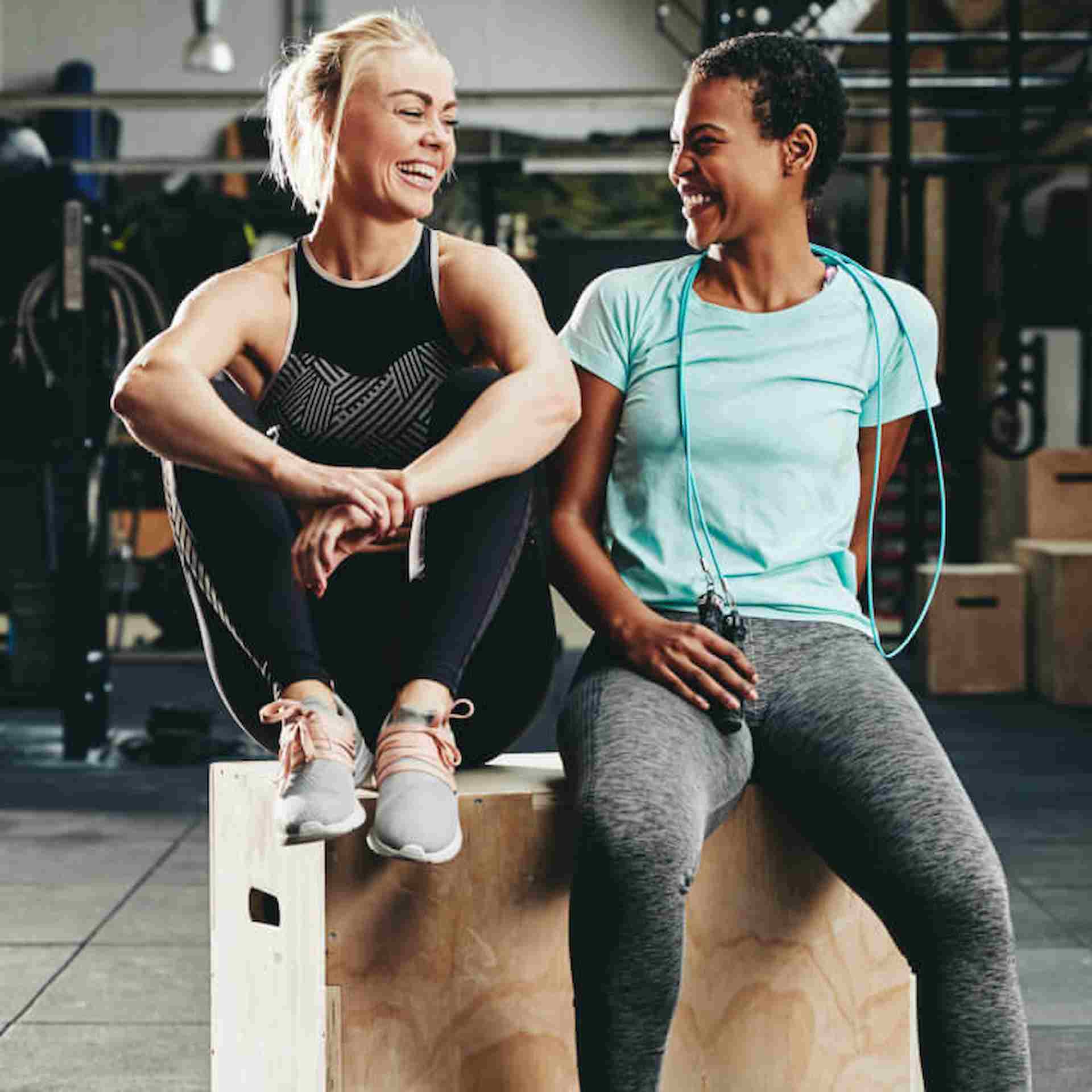 Two females sitting on a box in the gym laughing