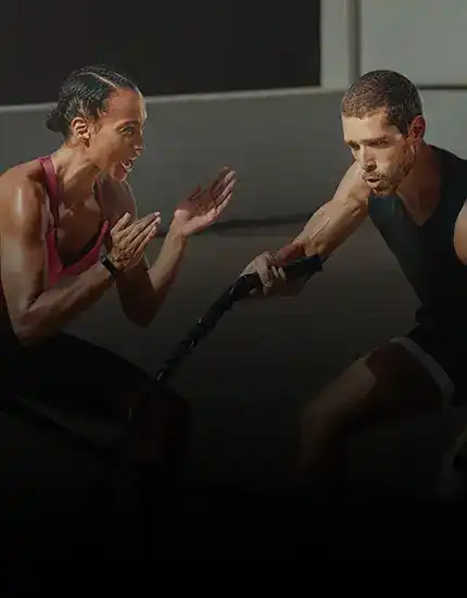 Female trainer coaching a male client doing battle ropes