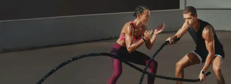 Female trainer coaching a male client doing battle ropes